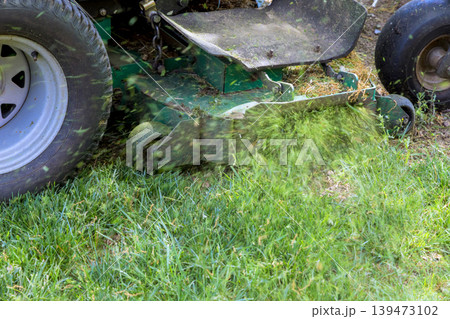 Lawnmower cuts grass in backyard while grass clippings scatter around 139473102