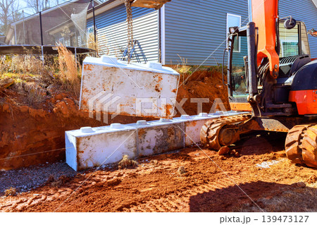 Excavator machine lifts large cement blocks of material at construction site for retaining walls Excavator machine lifts large cement blocks of material at construction site for retaining walls 139473127