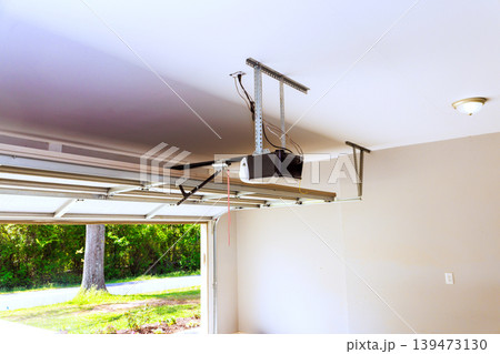 Garage door opener is mounted on ceiling, with door open, allowing to shine in. Garage door opener is mounted on ceiling, with door open, allowing to shine in. 139473130