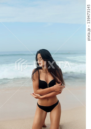 Beautiful woman in swimwear on the beach. Portrait of pretty female with slim tanned sexy body in black bikini . Summer lifestyle. Vacation 139473145