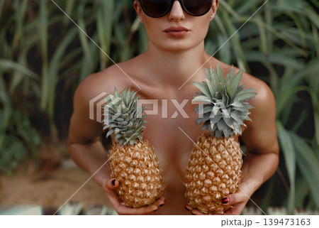 Beautiful Woman with bronze tan holds pineapples in hands Beautiful Woman with bronze tan holds pineapples in hands 139473163