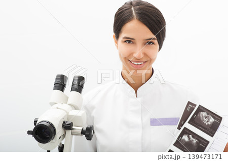 Portrait of a mixed race gynecologist sitting in an office near a colposcope. Gynecologist profession Portrait of a mixed race gynecologist sitting in an office near a colposcope. Gynecologist profession 139473171