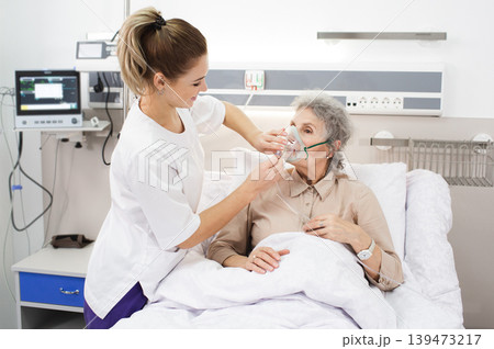 A nurse provides care to an elderly woman using a breathing mask in a medical clinic environment A nurse provides care to an elderly woman using a breathing mask in a medical clinic environment 139473217