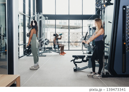 Women Training Together. Two Women Focusing On Fitness With Coaching And Friendly Interaction. Pair Of Women Working Out Near Cables With Trainer Providing Guidance And Encouragement Women Training Together. Two Women Focusing On Fitness With Coaching And Friendly Interaction. Pair Of Women Working Out Near Cables With Trainer Providing Guidance And Encouragement 139473341