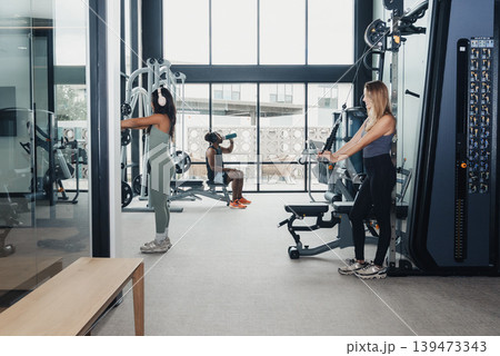 Ladies Converse While Working Out. Female Friends Gather And Talk During Fitness Session Breaks. Women Pause Their Workouts To Chat And Review Their Exercise Techniques Together 139473343