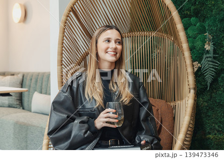 Smiling White Woman In Rattan Chair At Cozy Cafe Holding Glass Relaxed Creative Freelancer Taking Afternoon Break Amid Greenery And Neutral Decor Casual Fashion Candid Lifestyle Portrait Smiling White Woman In Rattan Chair At Cozy Cafe Holding Glass Relaxed Creative Freelancer Taking Afternoon Break Amid Greenery And Neutral Decor Casual Fashion Candid Lifestyle Portrait 139473346