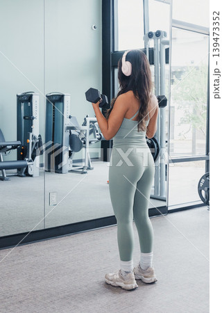 Woman Lifting Weights. Mirror Reflection Captures Woman In Workout Session. Secluded Gym Environment Highlights Woman Diligently Practicing Strength Training With Reflective Surface Woman Lifting Weights. Mirror Reflection Captures Woman In Workout Session. Secluded Gym Environment Highlights Woman Diligently Practicing Strength Training With Reflective Surface 139473352