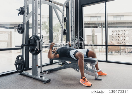 Athletic Training Session Underway. Performing Bench Press With Precision Focus. Male Athlete Performing Bench Press With Deliberate Rhythm And Proper Breathing Technique Athletic Training Session Underway. Performing Bench Press With Precision Focus. Male Athlete Performing Bench Press With Deliberate Rhythm And Proper Breathing Technique 139473354