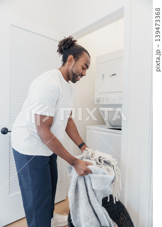 Black Man Loading Laundry Into Frontloader Washing Machine In Laundry Closet, Focused Domestic Chore, Casual Clothing, Basket With Towels, Efficient Routine And Everyday Household Black Man Loading Laundry Into Frontloader Washing Machine In Laundry Closet, Focused Domestic Chore, Casual Clothing, Basket With Towels, Efficient Routine And Everyday Household 139473368