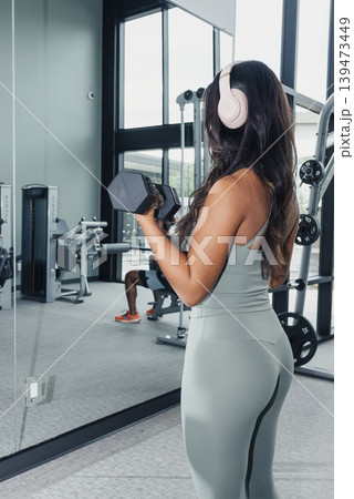 Focused Workout Imagery. Calm Studio Setting With Dedicated Woman Exercising Intelligently. An Athlete With Headphones Engaging In Focused Strength Training In Peaceful Studio Environment 139473449