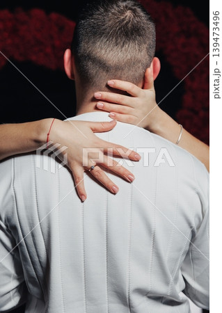 Man In White Suit Embraced Closely, Hands Clasped Around Neck, Wedding Band Visible, Dark Studio Backdrop With Highcontrast Lighting, Closeup Rear View Capturing Tactile Connection Man In White Suit Embraced Closely, Hands Clasped Around Neck, Wedding Band Visible, Dark Studio Backdrop With Highcontrast Lighting, Closeup Rear View Capturing Tactile Connection 139473496