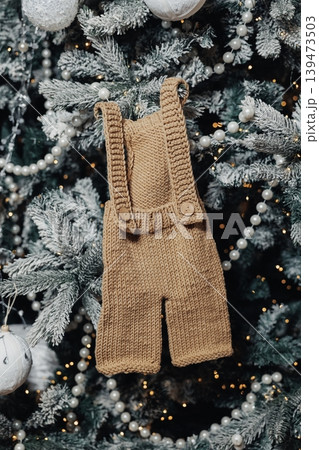 Knitted Baby Romper Hanging On Tree, Flocked Branches And Pearl Garland, Warm Fairy Lights And Soft Bokeh, Handcrafted Neutral Ornament Evokes Cozy Holiday Reveal And Gift Inspiration Knitted Baby Romper Hanging On Tree, Flocked Branches And Pearl Garland, Warm Fairy Lights And Soft Bokeh, Handcrafted Neutral Ornament Evokes Cozy Holiday Reveal And Gift Inspiration 139473503