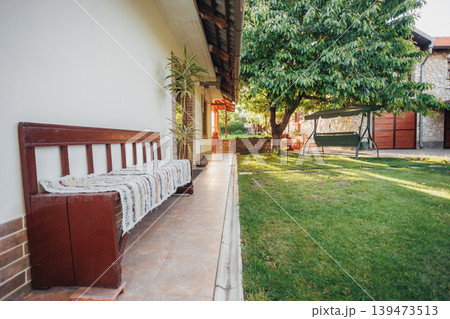 Textured Porch Bench With Patterned Cushions And Hanging Plant, Narrow Walkway Leading To Yard Framed By Warm Light Shot Tailored For Home Decor, Porch Styling, Architectural Detail 139473513