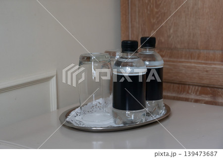 Two bottled waters, glass on tray in hotel room interior with clean minimalist arrangement on table. Hospitality service, travel accommodation, hotel amenities, guest comfort, lifestyle Two bottled waters, glass on tray in hotel room interior with clean minimalist arrangement on table. Hospitality service, travel accommodation, hotel amenities, guest comfort, lifestyle 139473687