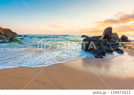 huge stones on the sandy beach at sunrise. wonderful holiday season background at the sea. clouds on the blue sky above horizon. view of waves washing the shore. scenic seascape for relaxation huge stones on the sandy beach at sunrise. wonderful holiday season background at the sea. clouds on the blue sky above horizon. view of waves washing the shore. scenic seascape for relaxation 139473811