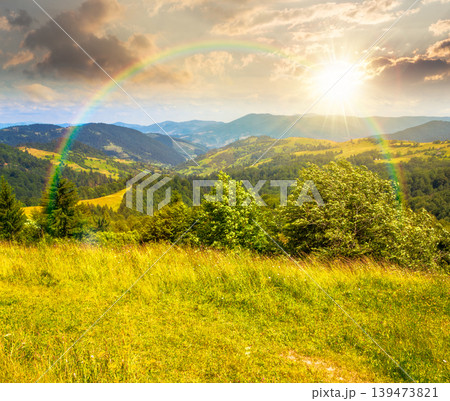 sunset over agricultural field on hillside in mountains near village. carpathian mountain landscape in summer. countryside view of alpine fields and rolling hills. cloudy sky with rainbow sunset over agricultural field on hillside in mountains near village. carpathian mountain landscape in summer. countryside view of alpine fields and rolling hills. cloudy sky with rainbow 139473821