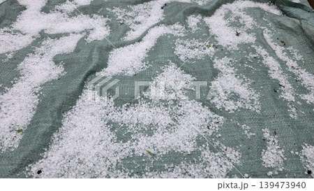 Hailstones covering green garden protective mesh after severe spring storm, close up of ice balls on textured surface. Concept of weather damage and garden protection 139473940