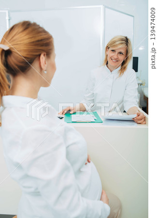 Smiling obstetrician talking with pregnant woman in clinic examination room Smiling obstetrician talking with pregnant woman in clinic examination room 139474009