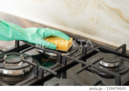 Cleaning a gas hob with a sponge and glove, removing grease in a modern kitchen. 139474043