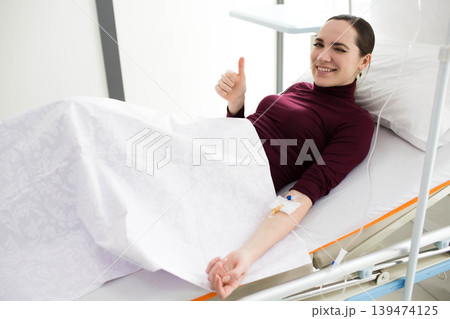 Woman lying in hospital bed, patient recovery , Feeling better after IV Drip treatment Woman lying in hospital bed, patient recovery , Feeling better after IV Drip treatment 139474125