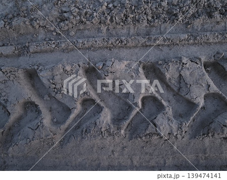 Close-up of deep tire tread mark on dry sandy ground with rough texture under natural light. Concept of off-road transportation and heavy machinery impact Close-up of deep tire tread mark on dry sandy ground with rough texture under natural light. Concept of off-road transportation and heavy machinery impact 139474141