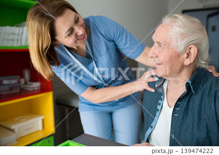 Happy caretaker assisting senior man. Friendly nurse supporting old man with Parkinson's Disease Happy caretaker assisting senior man. Friendly nurse supporting old man with Parkinson's Disease 139474222