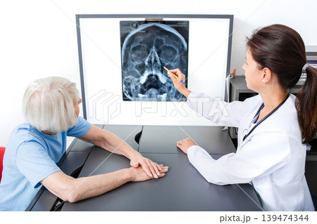 Doctor consider and discuss with senior patient X-ray of her head and maxillary sinuses. Diagnostics and treatment of sinusitis and frontal sinusitis Doctor consider and discuss with senior patient X-ray of her head and maxillary sinuses. Diagnostics and treatment of sinusitis and frontal sinusitis 139474344