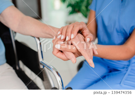 Medical support patient in a wheelchair. Close-up of hands of a healthcare worker and an elderly person with a disability taking care of a patient 139474356