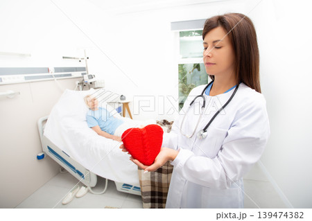 Care for an elderly patient in a hospital. Doctor holding a heart model. Cardiology, medical care for patients with heart disease. Heart attack, treatment, and recovery Care for an elderly patient in a hospital. Doctor holding a heart model. Cardiology, medical care for patients with heart disease. Heart attack, treatment, and recovery 139474382