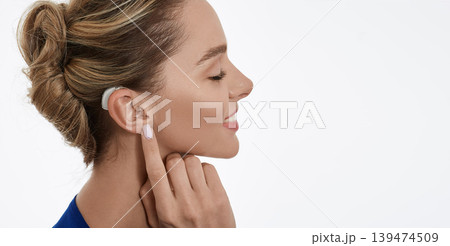 Positive woman with hearing aid behind her ear enjoying her hearing restoration, isolated on white. Hearing aids Positive woman with hearing aid behind her ear enjoying her hearing restoration, isolated on white. Hearing aids 139474509