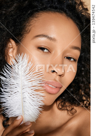 Facial skin care. African American woman showing smooth and soft her skin is by touching her face with white feather Facial skin care. African American woman showing smooth and soft her skin is by touching her face with white feather 139474542