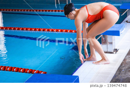 Female professional swimmer getting ready to jump in swimming pool of starting position. Jumping in a swimming pool, training Female professional swimmer getting ready to jump in swimming pool of starting position. Jumping in a swimming pool, training 139474748
