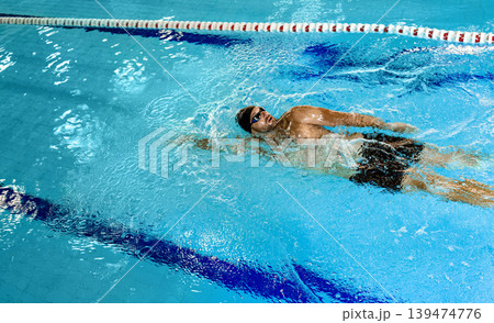 Man swimmer is swimming in the pool, backstroke technique swimming. Shot of swim in motion, top view Man swimmer is swimming in the pool, backstroke technique swimming. Shot of swim in motion, top view 139474776