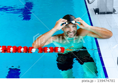 Portrait of a positive professional swimmer in a pool wearing swimming goggles, resting after swimming in the pool 139474781