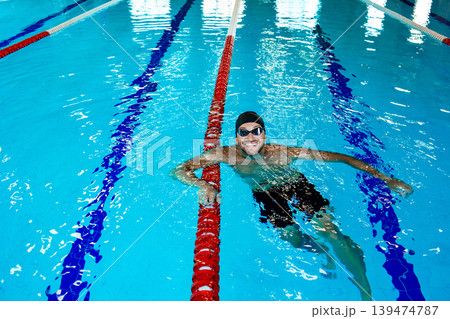 Portrait of a positive professional swimmer in a pool resting after swimming in the pool. Swimming training Portrait of a positive professional swimmer in a pool resting after swimming in the pool. Swimming training 139474787