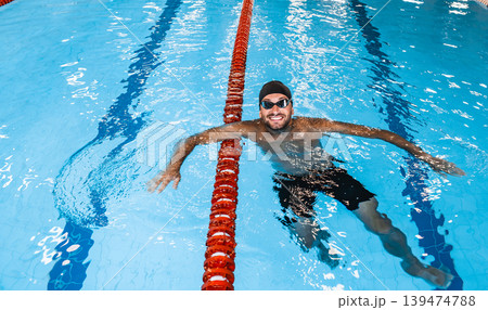 Portrait of a positive professional swimmer in a pool resting after swimming in the pool. Swimming training Portrait of a positive professional swimmer in a pool resting after swimming in the pool. Swimming training 139474788