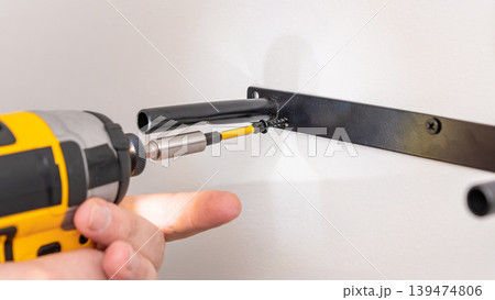 Mans hands using yellow cordless drill with extension to fasten screw into wall bracket. Home improvement, installing support, DIY extension use, precise fastening. Mans hands using yellow cordless drill with extension to fasten screw into wall bracket. Home improvement, installing support, DIY extension use, precise fastening. 139474806