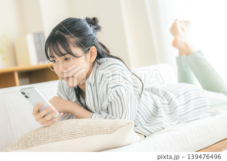 寝転んでスマホを見る眼鏡の女性 寝転んでスマホを見る眼鏡の女性 139476496