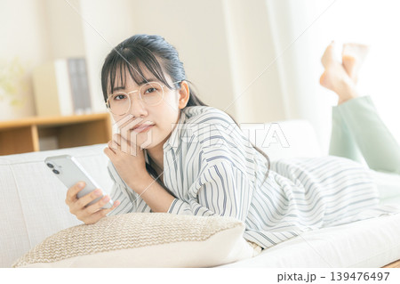 寝転んでスマホを見る眼鏡の女性 寝転んでスマホを見る眼鏡の女性 139476497