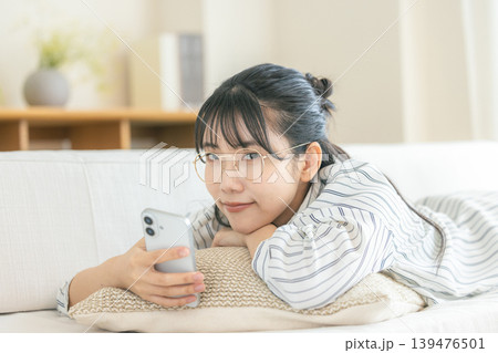 寝転んでスマホを見る眼鏡の女性 寝転んでスマホを見る眼鏡の女性 139476501