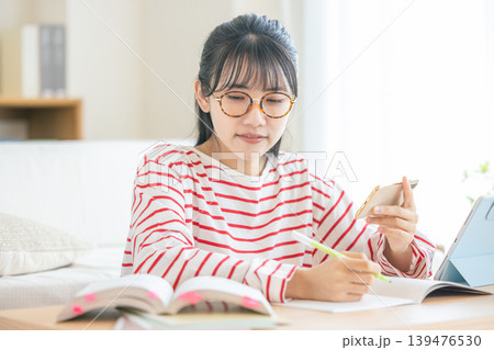 スマホを見ながら勉強する若い女性 スマホを見ながら勉強する若い女性 139476530