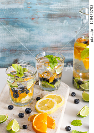 Summer healthy cocktails of citrus infused waters, lemonades or mojitos, with lime lemon orange blueberries and mint, diet detox beverages, in glasses on light background 139476792