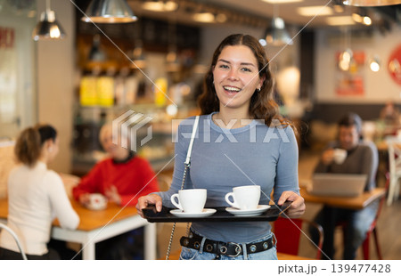 Girl visitor in self-service cafeteria carries tray with two cups of coffee. Girl visitor in self-service cafeteria carries tray with two cups of coffee. 139477428