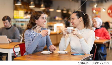Girlfriends are chatting happily with each other while sitting at table in a cafe and drinking tea Girlfriends are chatting happily with each other while sitting at table in a cafe and drinking tea 139477509