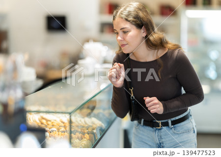 Young woman in casual clothes choosing sweet pastries at pastry shop display Young woman in casual clothes choosing sweet pastries at pastry shop display 139477523