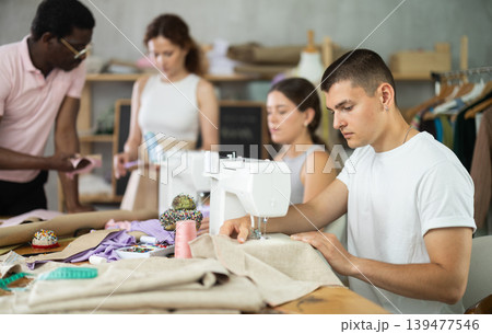 Engaged guy stitching fabric on machine in sewing class for adults Engaged guy stitching fabric on machine in sewing class for adults 139477546