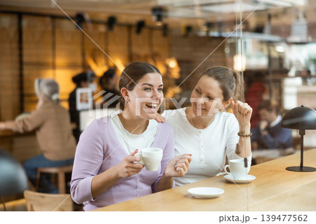 Two cheerful women chatting and drinking coffee at the bar counter of cafe Two cheerful women chatting and drinking coffee at the bar counter of cafe 139477562