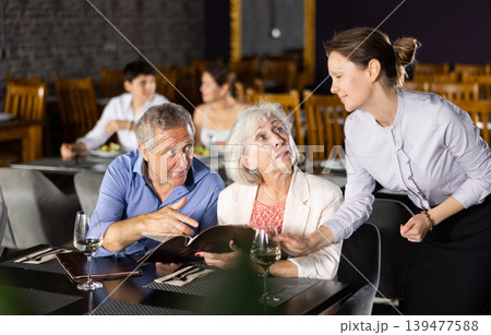 Woman waiter taking order from elderly couple in restaurant Woman waiter taking order from elderly couple in restaurant 139477588