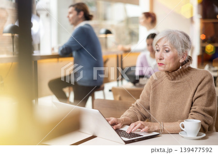 Mature woman spending time in cozy coffeehouse with laptop and coffee Mature woman spending time in cozy coffeehouse with laptop and coffee 139477592