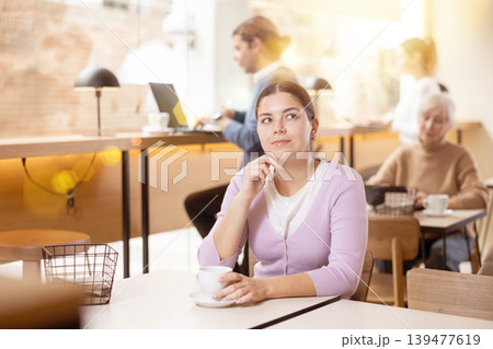 Dreamy young girl drinking coffee in cozy cafe Dreamy young girl drinking coffee in cozy cafe 139477619
